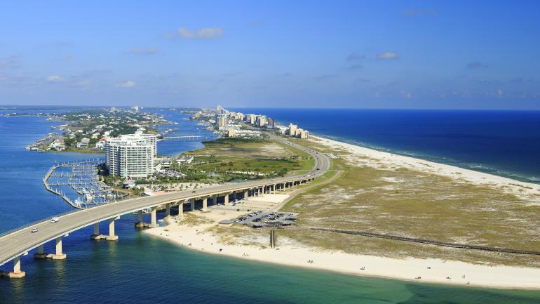 Roadway crossing over the water and alongside white-sand beaches in Gulf Shores, Alabama