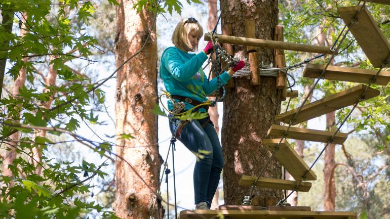 一位女性正准备穿过 Go Ape Treetop Adventure 冒险乐园绳索项目场地中的曲桥 一位女性正准备穿过 Go Ape Treetop Adventure 冒险乐园绳索项目场地中的曲桥