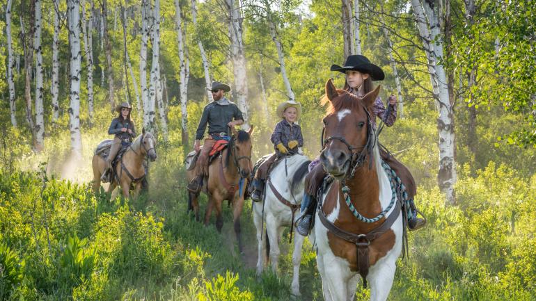 A family riding horses on a Colorado dude ranch trail