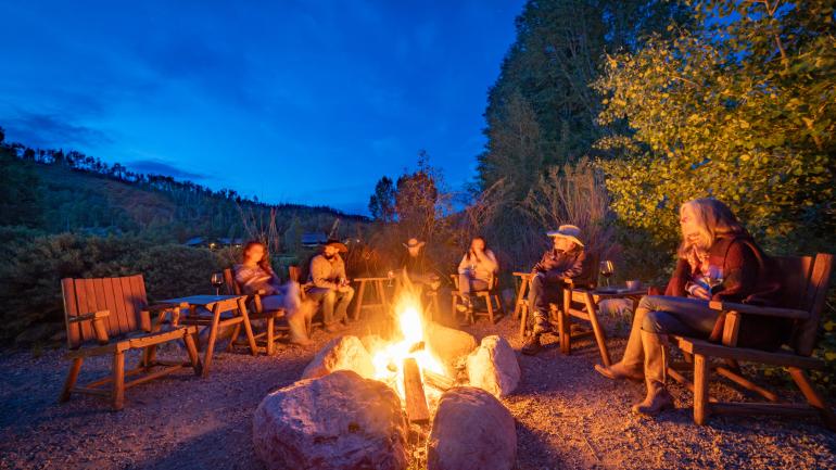 Dude ranch guests having evening drinks around a campfire