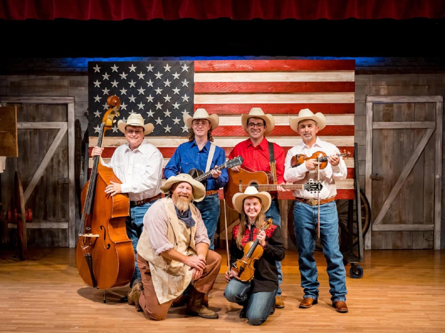 在密苏里州布兰森，The Great American Chuckwagon Dinner Show 晚餐表演的表演者们在美国国旗前拍照留念